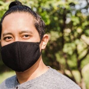 A man wearing a black mask standing in front of trees.