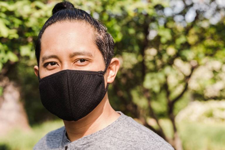 A man wearing a black mask standing in front of trees.